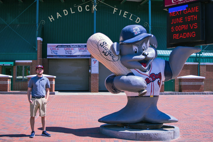 Sport management major Will Highland standing outside of the Hadlock Field gates next to a sculpture of the Sea Dogs' mascot. 