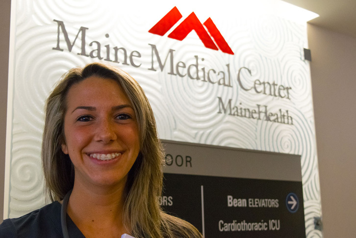 A female Colby-Sawyer nursing student smiles next to a sign for Maine Medical Center.