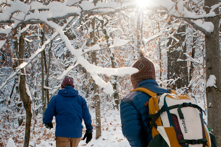 Two Colby-Sawyer students hiking on snow covered trail in the forest.